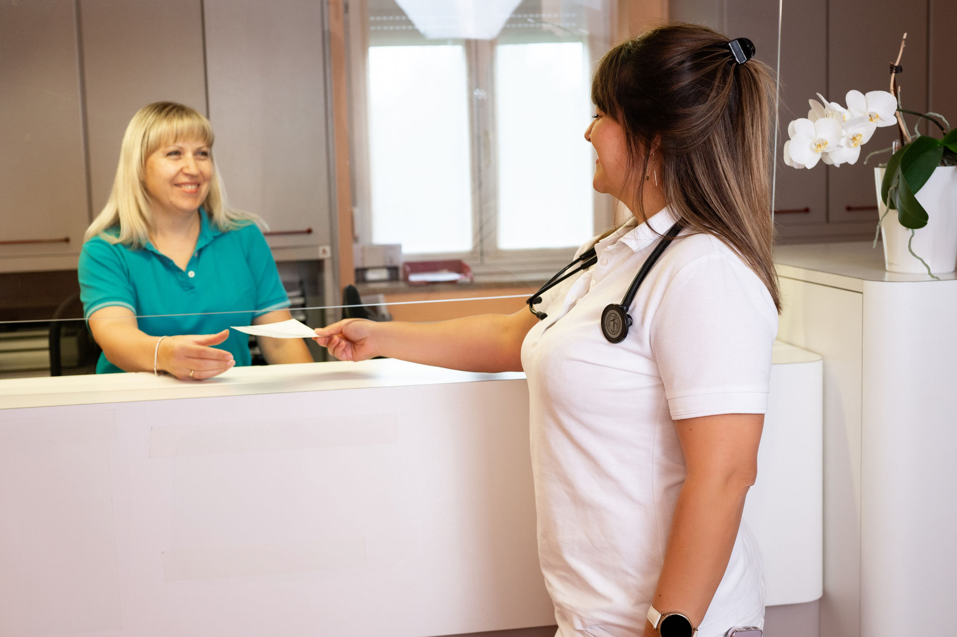 Die Ärztin gibt ihrer Praxismanagerin ein Dokument.